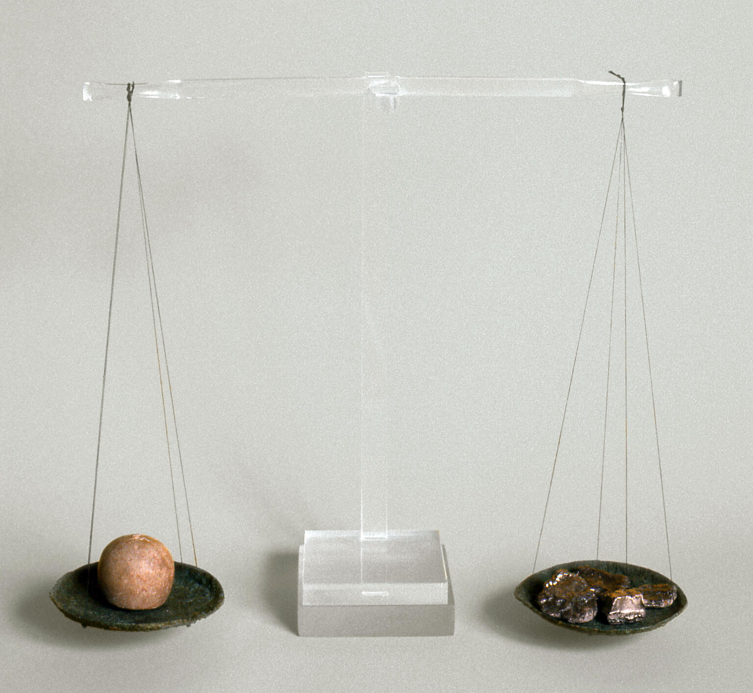 Reconstructed scale with two ancient bronze pans suspended from central beam of clear modern material. The left pan holds a balance weight and the right holds a piece of silver.