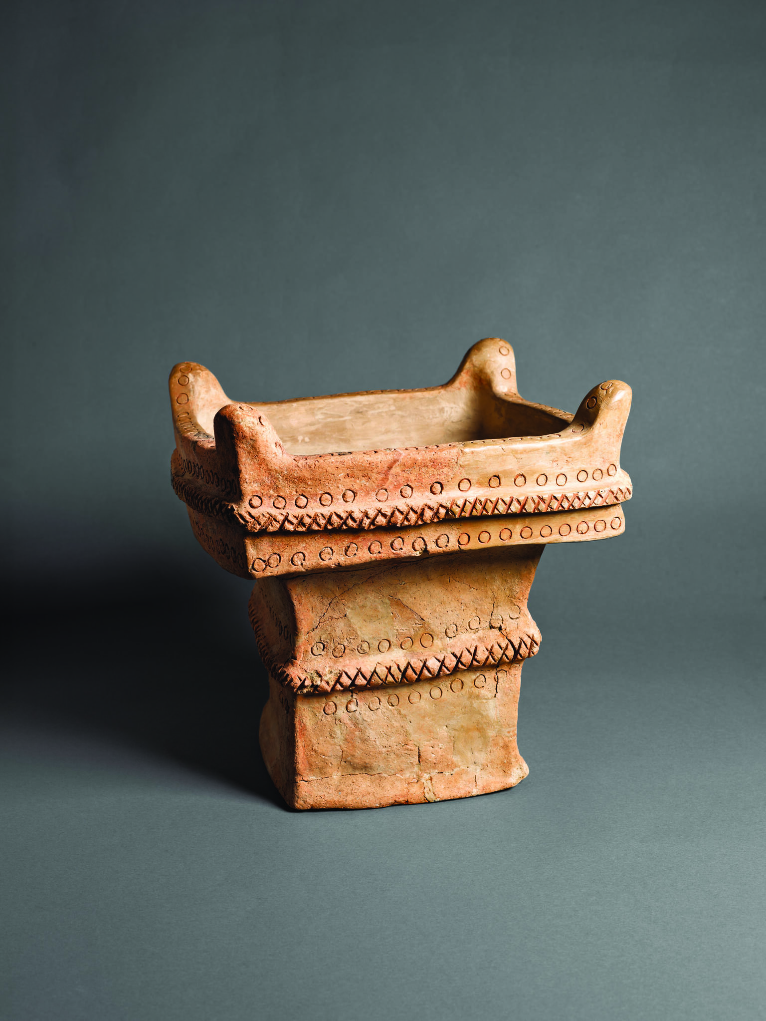 Square ceramic altar with recessed offering surface decorated with crosshatching and circles and horns on four upper corners.