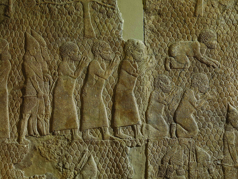 Wall relief showing six men dressed in tunics, one prostrate and two kneeling, with two bearded soldiers behind them.