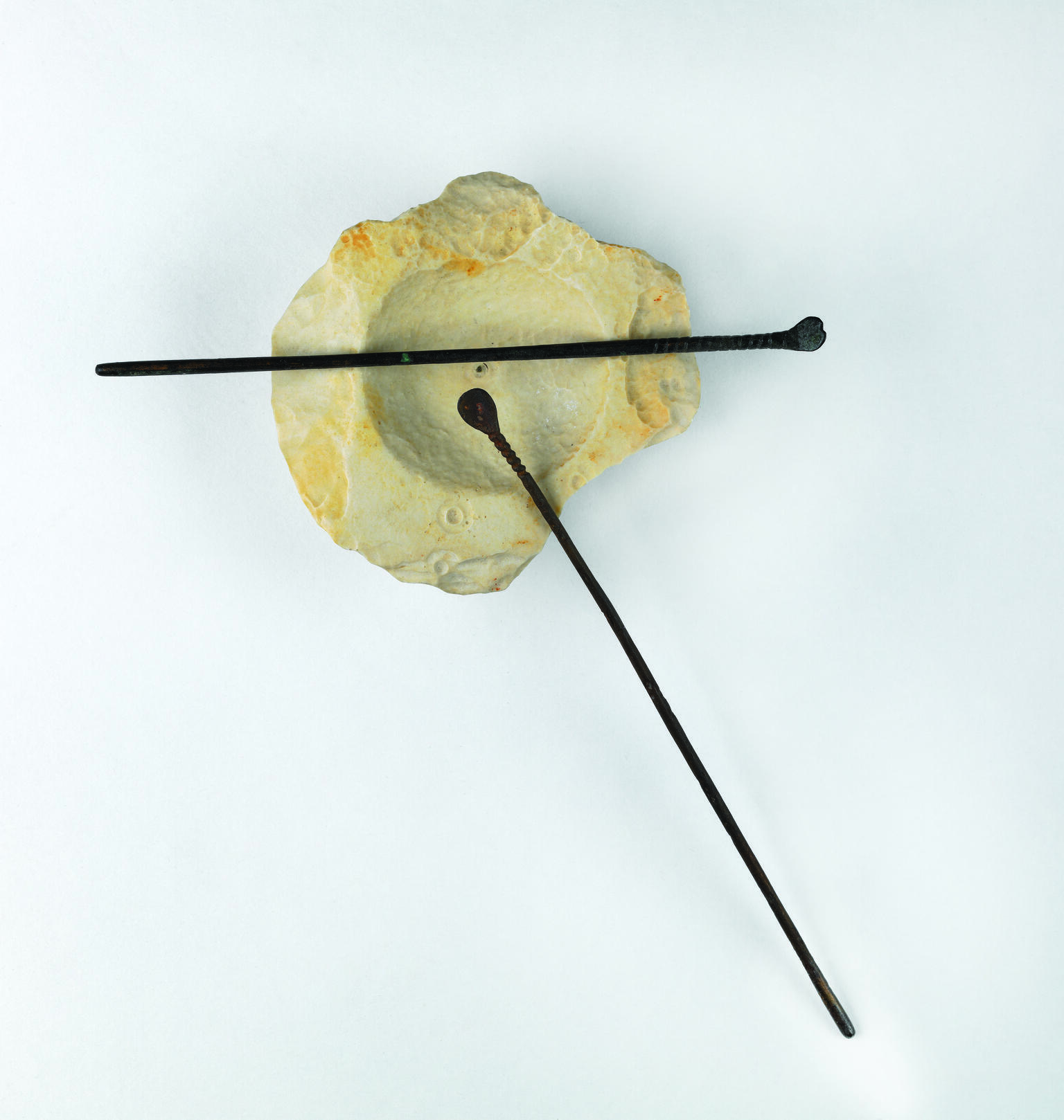 Limestone bowl and two small bronze spatulas resting on it.