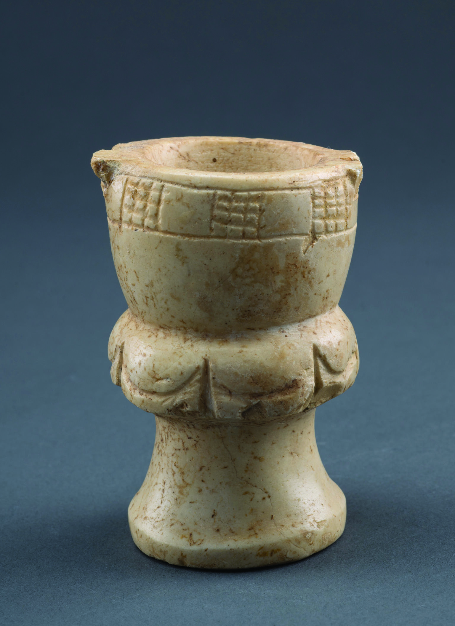 Limestone, goblet-shaped container with a footed base, a midsection with festoon pattern, and a deep bowl with checkerboard pattern on rim.