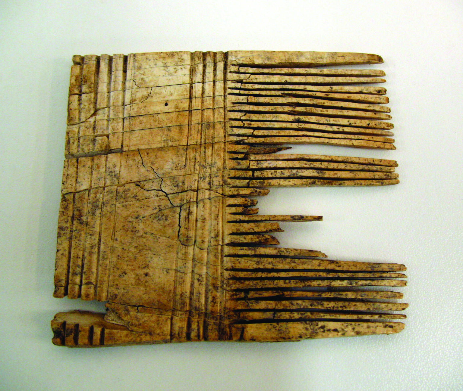 Square-shaped comb with closely-positioned teeth on the right-hand side and wide handle with carved stripes.