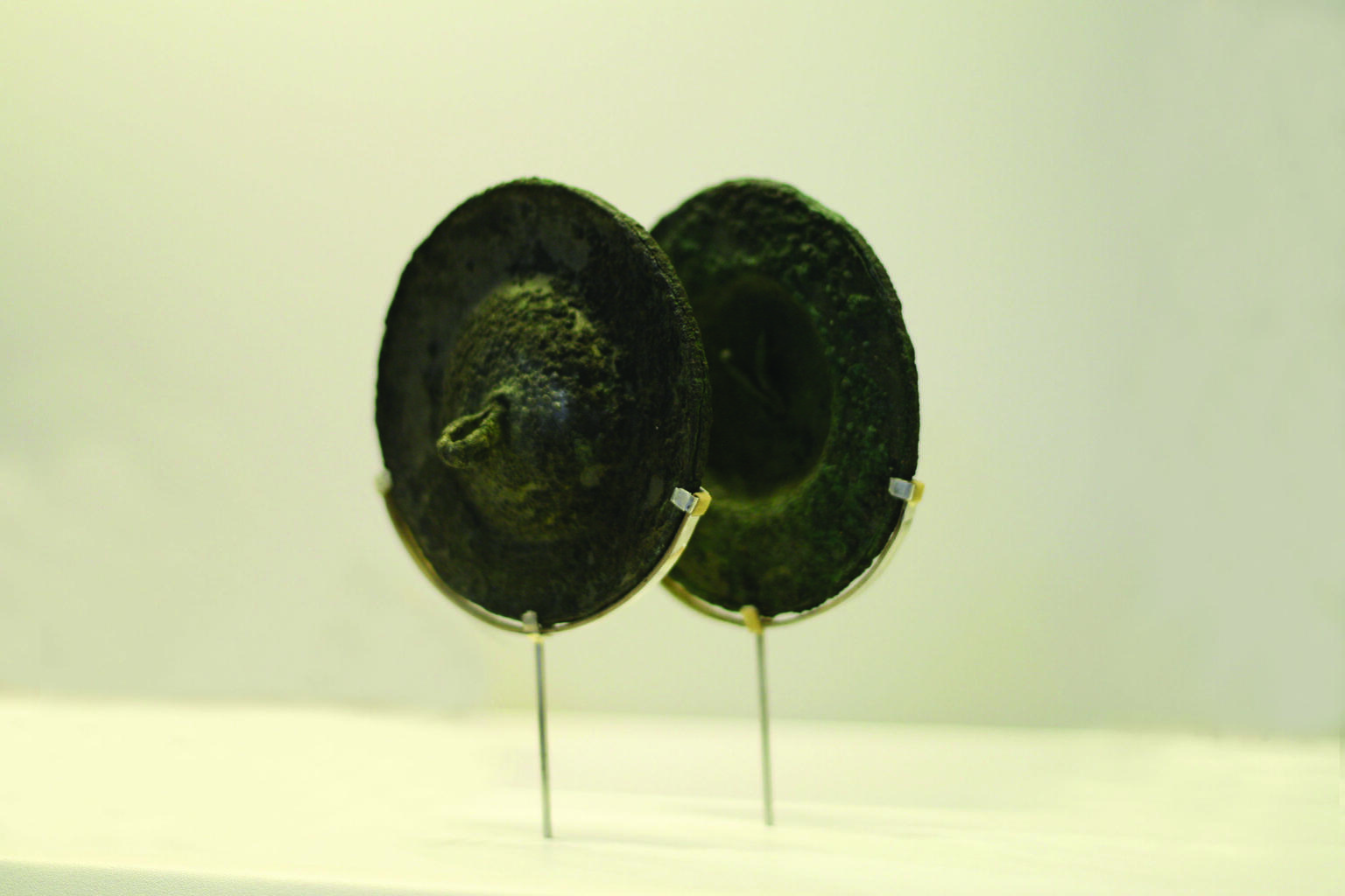 Pair of round bronze cymbals set on a modern wire display frame. 