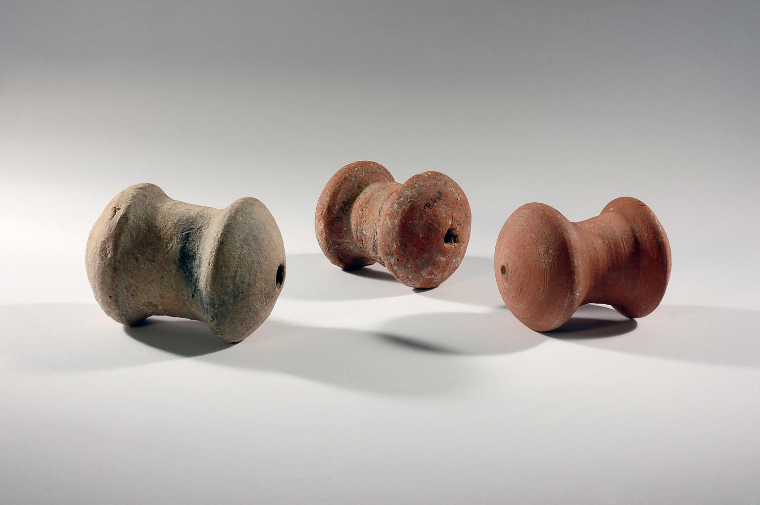 Three spool-shaped terra-cotta objects with a hole on one end.