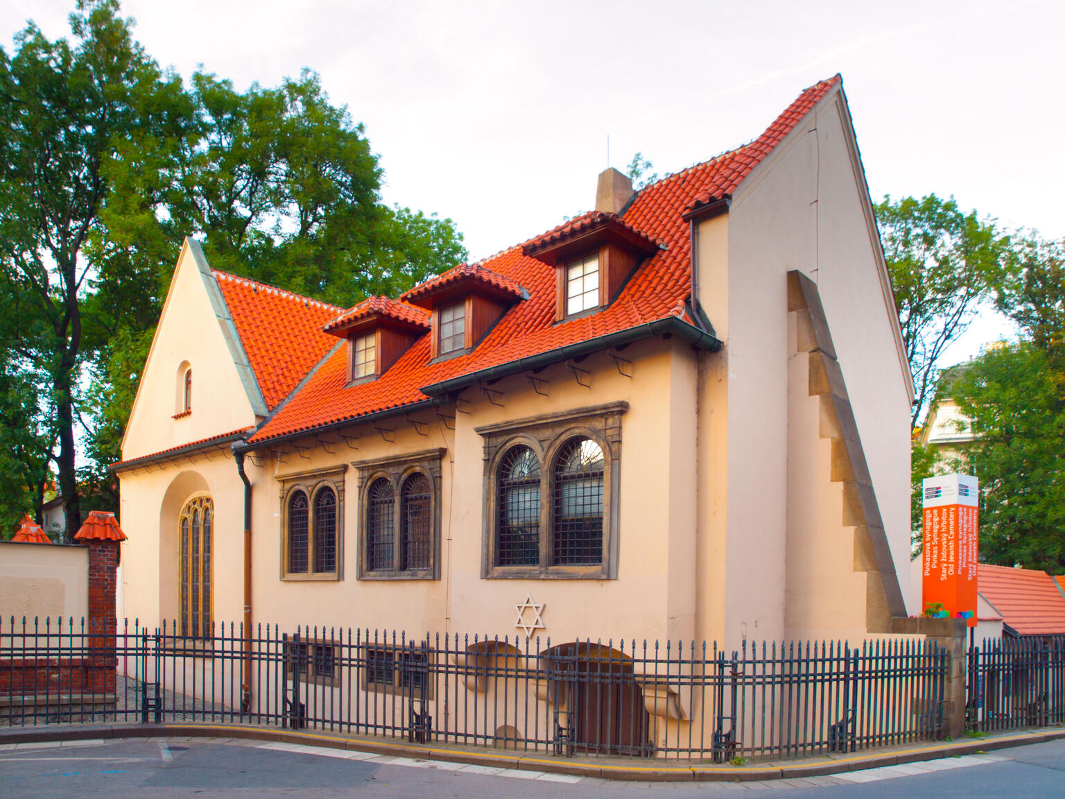 Front view of building exterior with curved tile roof and arched windows and metal fence around perimeter. 