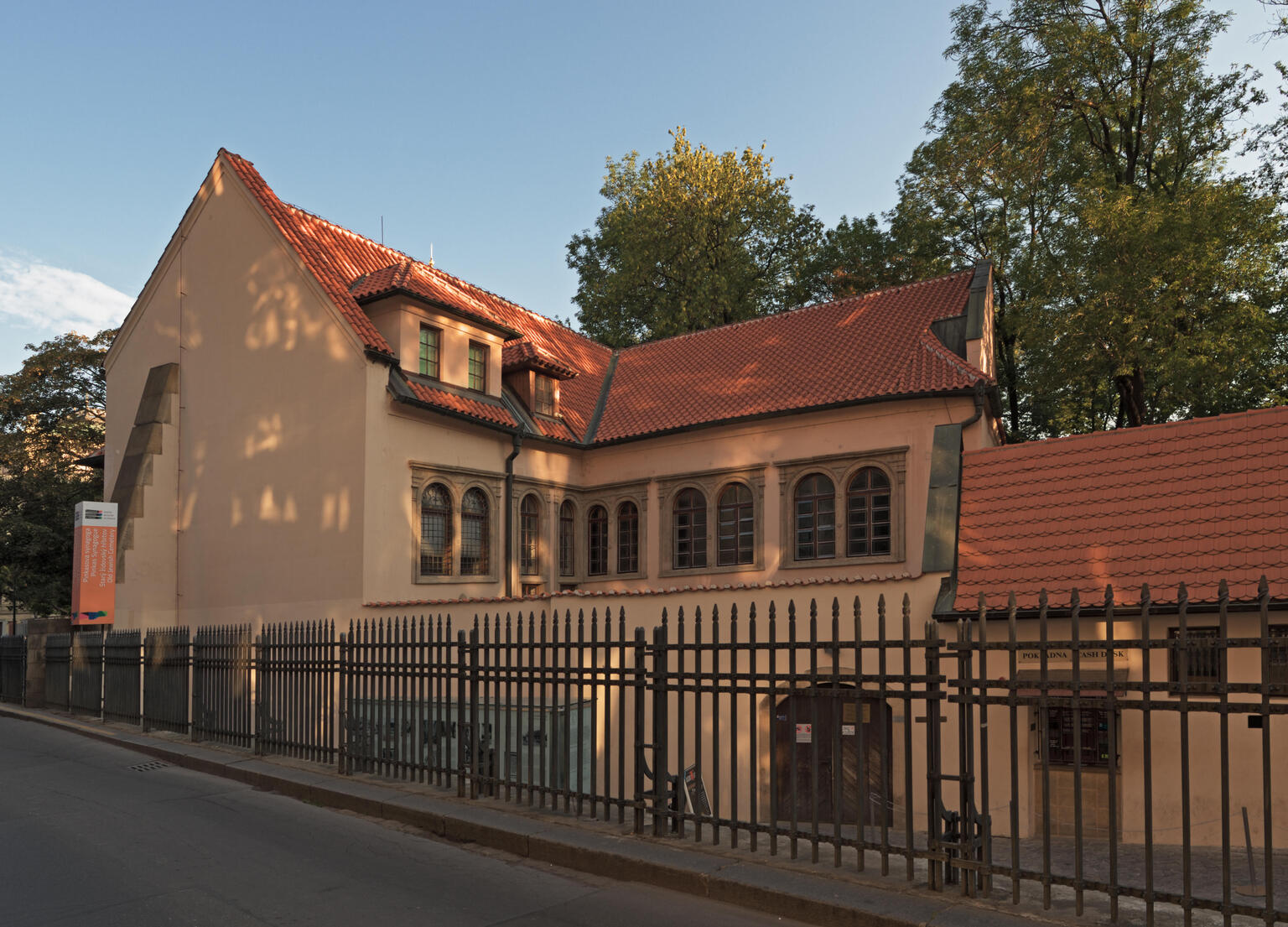 Rear view of exterior building with curved tile roof, arched windows and metal fence around perimeter. 