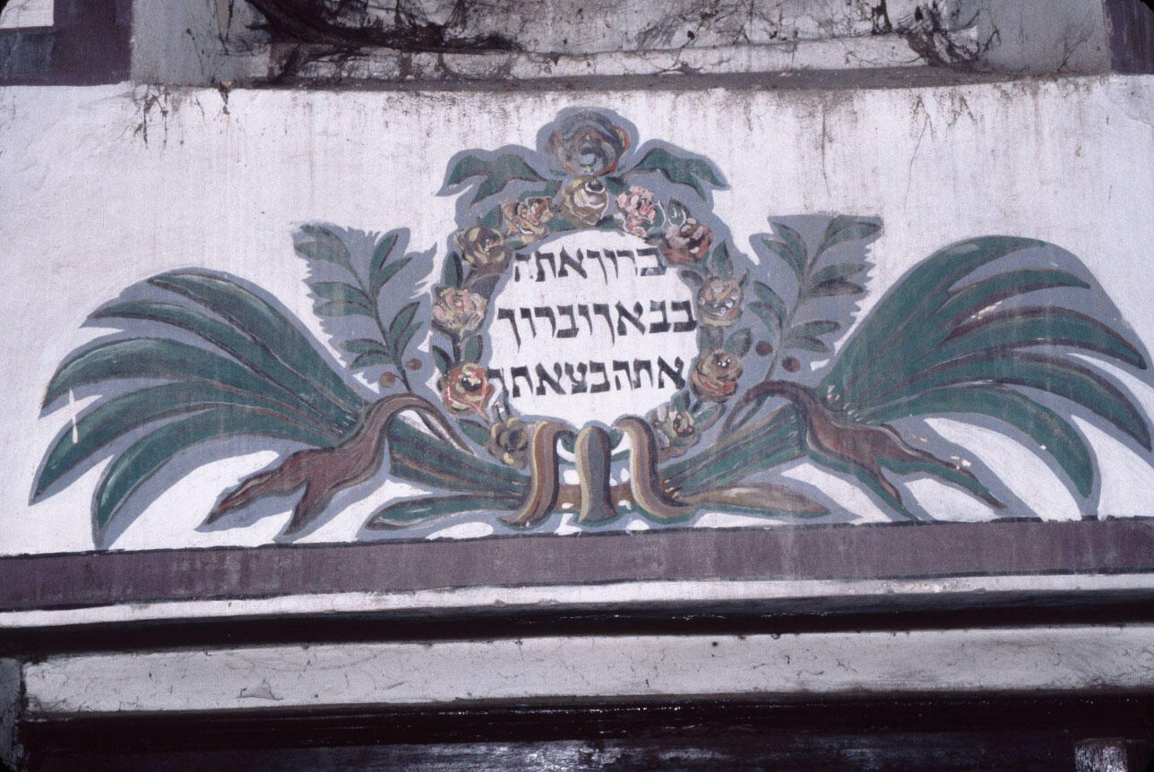 Photograph of Hebrew text in decorated frame with plumage. 