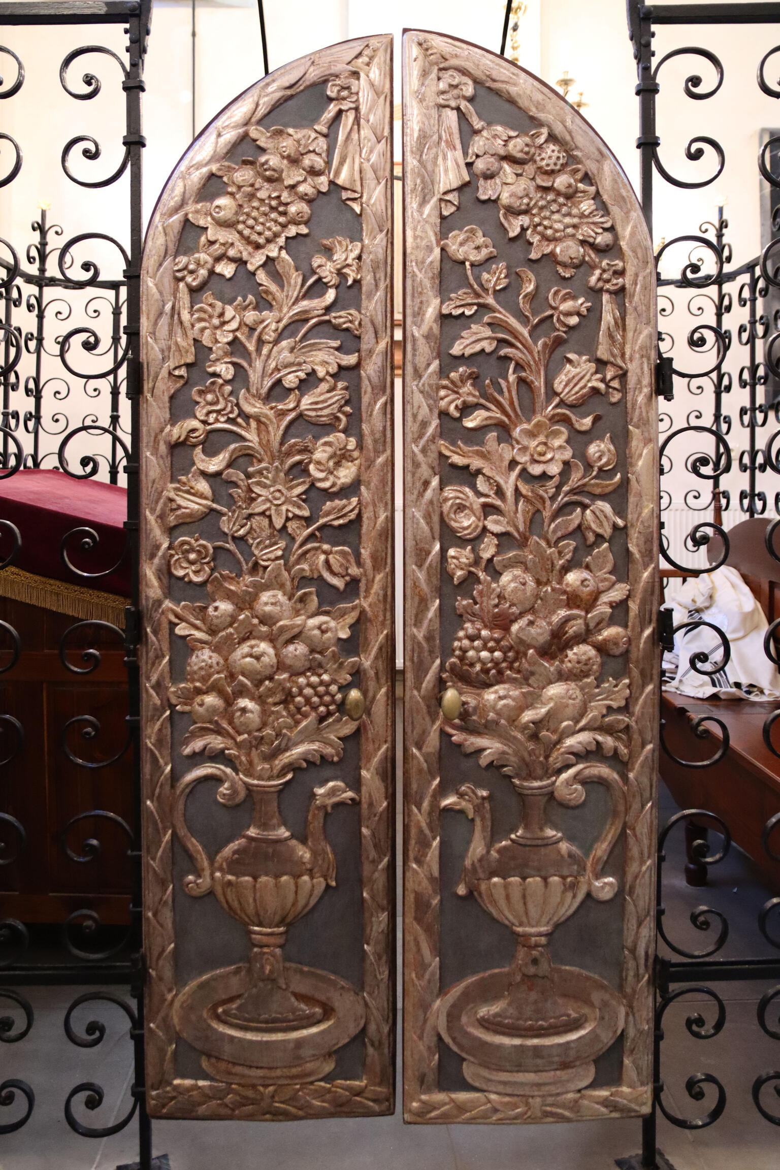 Set of curved doors with carving of peacock-shaped pitcher filled with foliage and fruit extending to top of door. 
