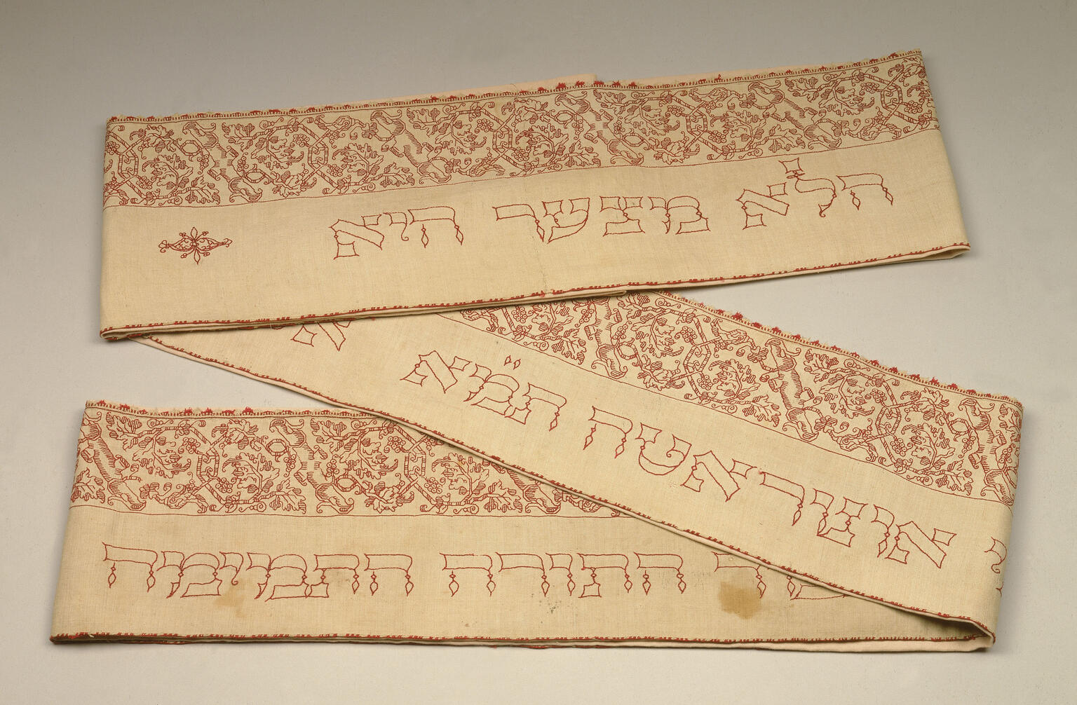 Rectangular cloth, folded in two places, with Hebrew text embroidered on bottom half of cloth and floral border on top half. 