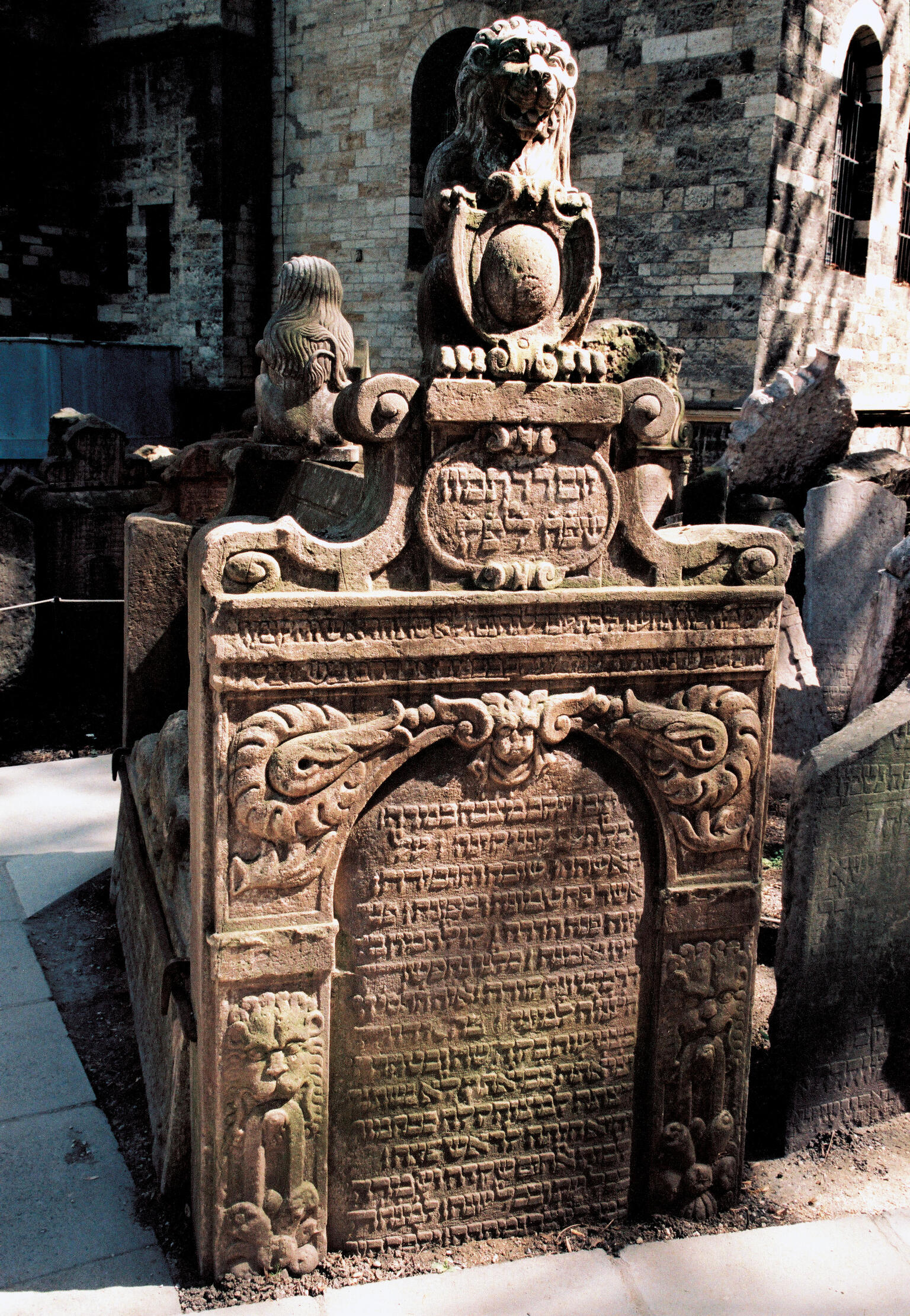 Tomb with high tombstones on either end, lions, shield and floral decorations on top, and Hebrew inscription on surface of stone.
