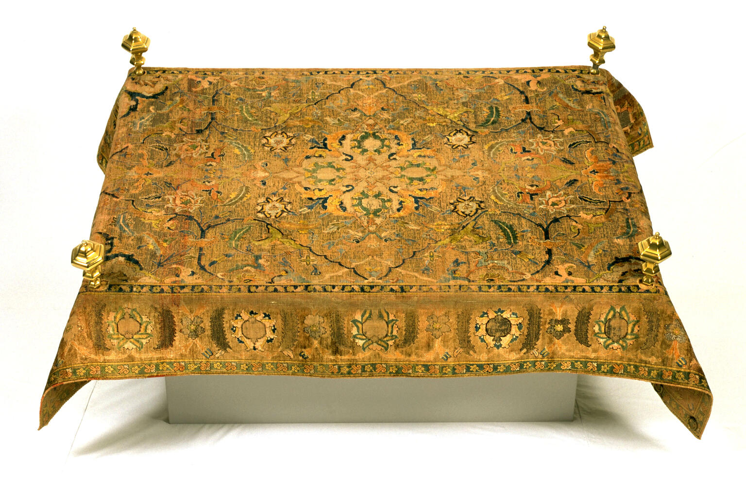 Carpet with embroidered designs and four small posts near each corner. 
