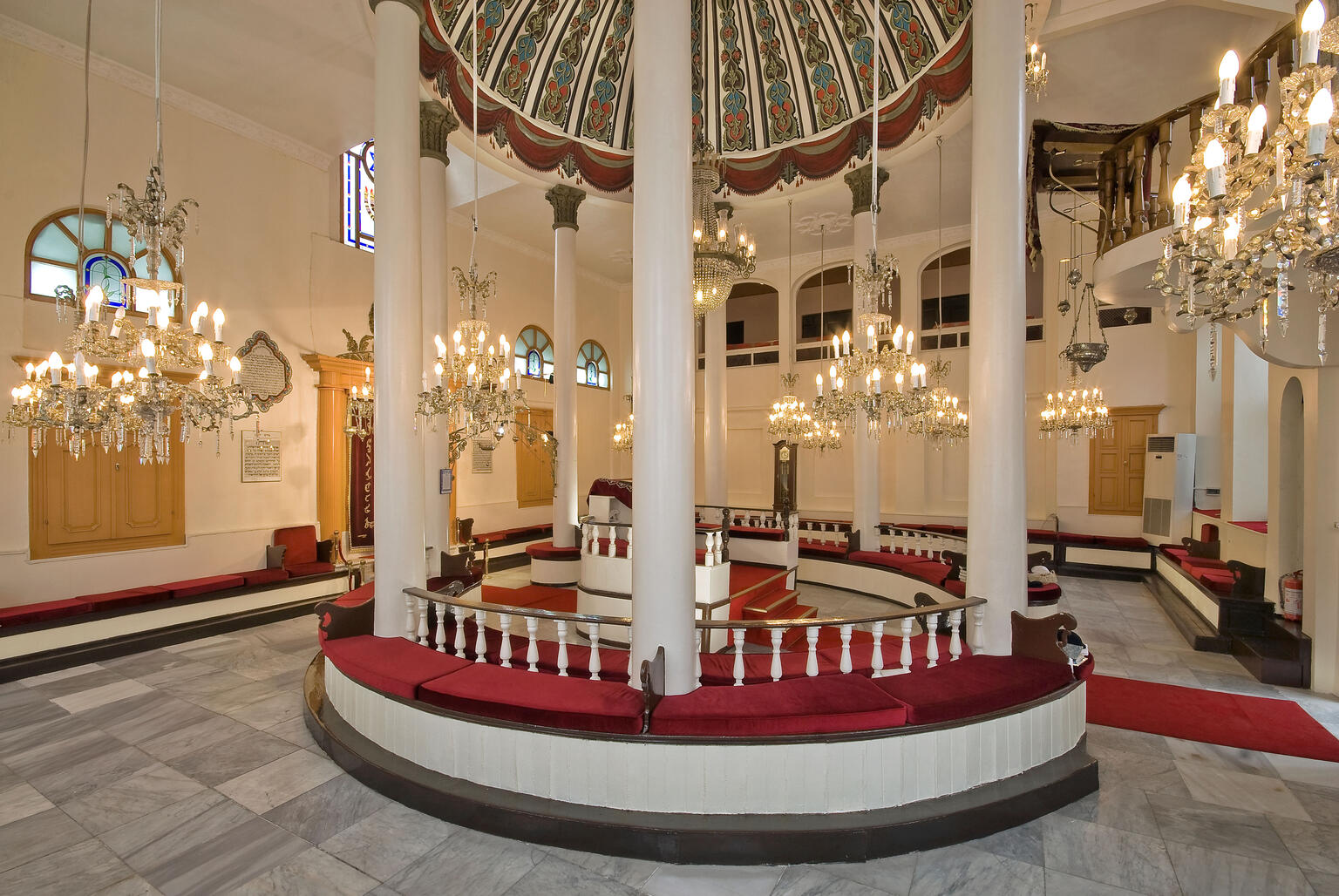 Room interior with central podium with tall columns and many chandeliers surrounding.