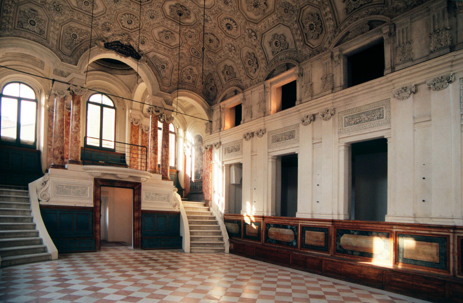 Interior of room with columns and short double staircase at one end and pews along wall. Interior of room with columns and short double staircase at one end and pews along wall.