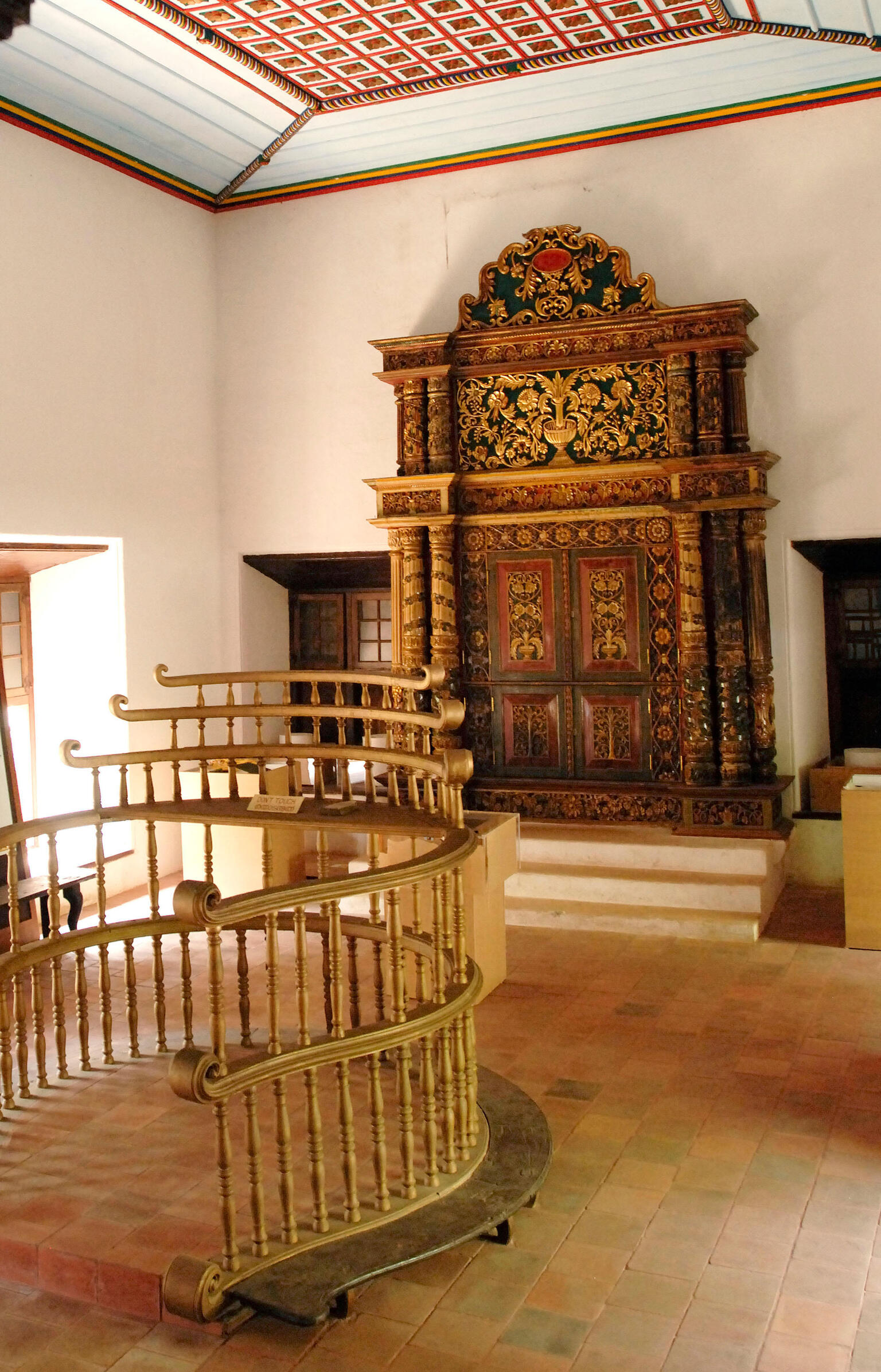 Photograph of room with raised platform with railings in center and carved wooden Torah chamber on back wall. Photograph of room with raised platform with railings in center and carved wooden Torah chamber on back wall.