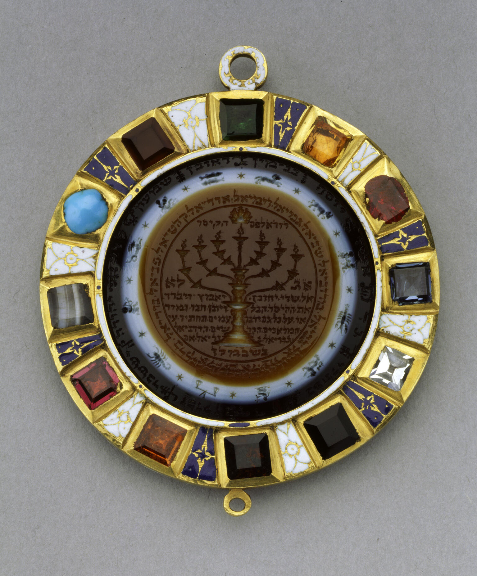 Circular amulet with stones around perimeter and image of candelabrum with Hebrew text in center, surrounded by images of the zodiac. Circular amulet with stones around perimeter and image of candelabrum with Hebrew text in center, surrounded by images of the zodiac.