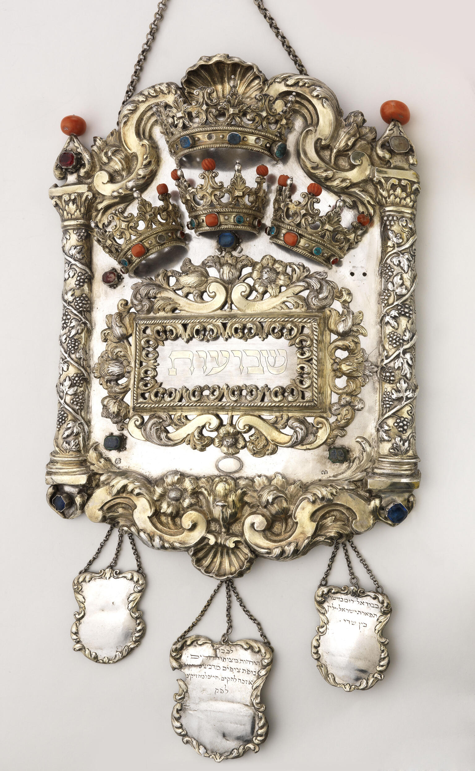 Torah shield decorated with vine-wrapped columns on either side, crowns across the top, and three smaller shields hanging from bottom. Torah shield decorated with vine-wrapped columns on either side, crowns across the top, and three smaller shields hanging from bottom.