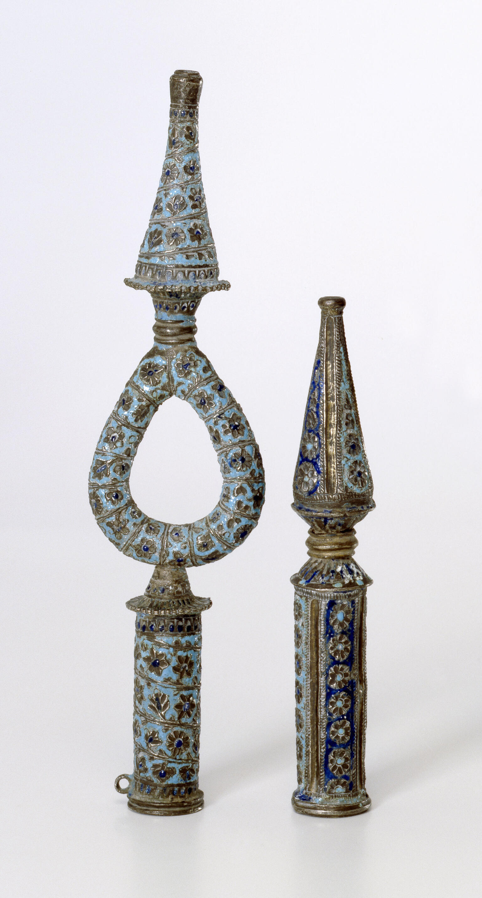 Two finials, one with a loop in the middle, decorated with flowers and lines.