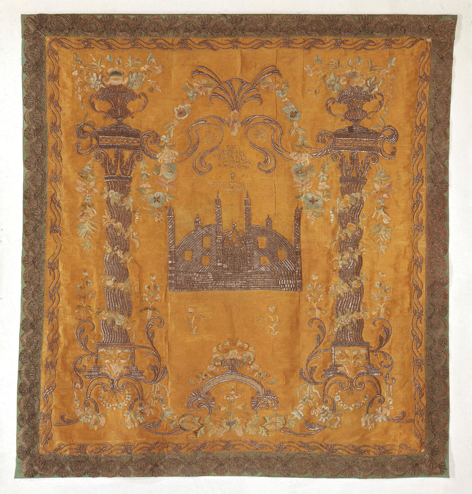Cloth embroidered with columns on either side and building in the middle with turrets and dome, with small Hebrew inscription above. 