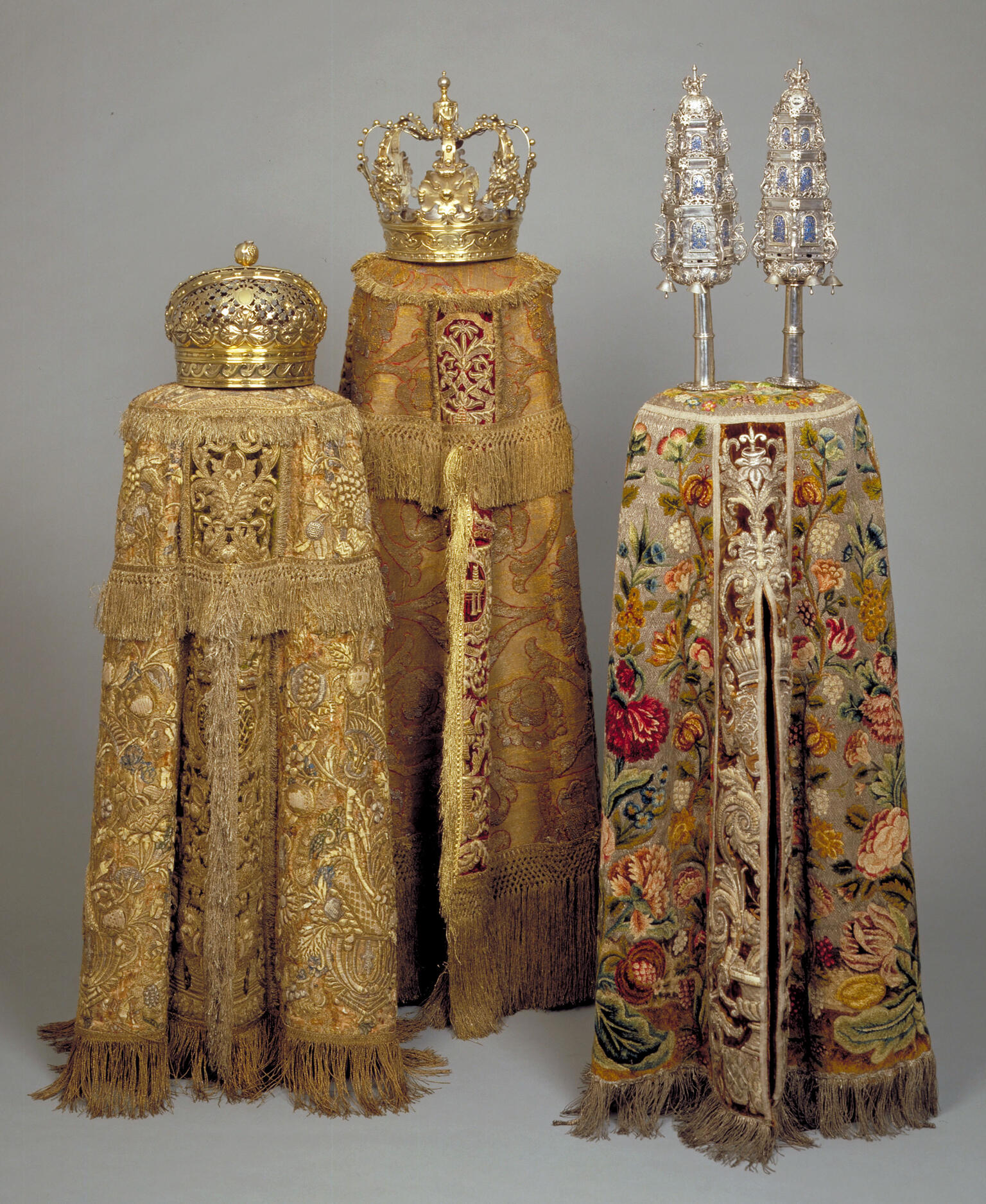 Three cylindrical embroidered cloth covers, two with crowns on top and one with two finials on top. 