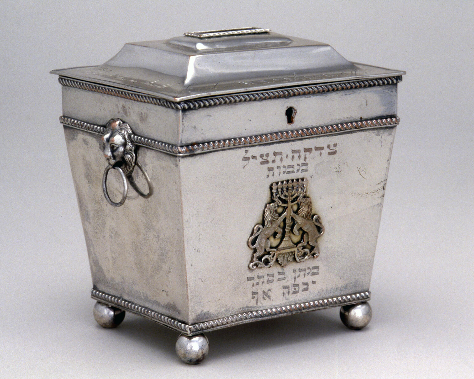 Silver cast and engraved container featuring lions holding menorah.