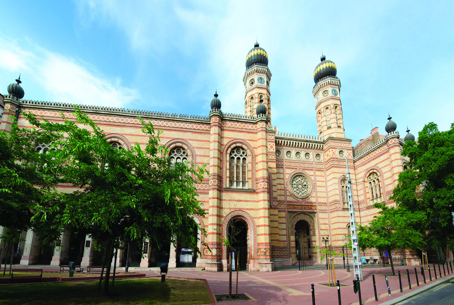 Photograph of exterior facade of building with minarets, circular windows, and decoration, and trees in courtyard. 