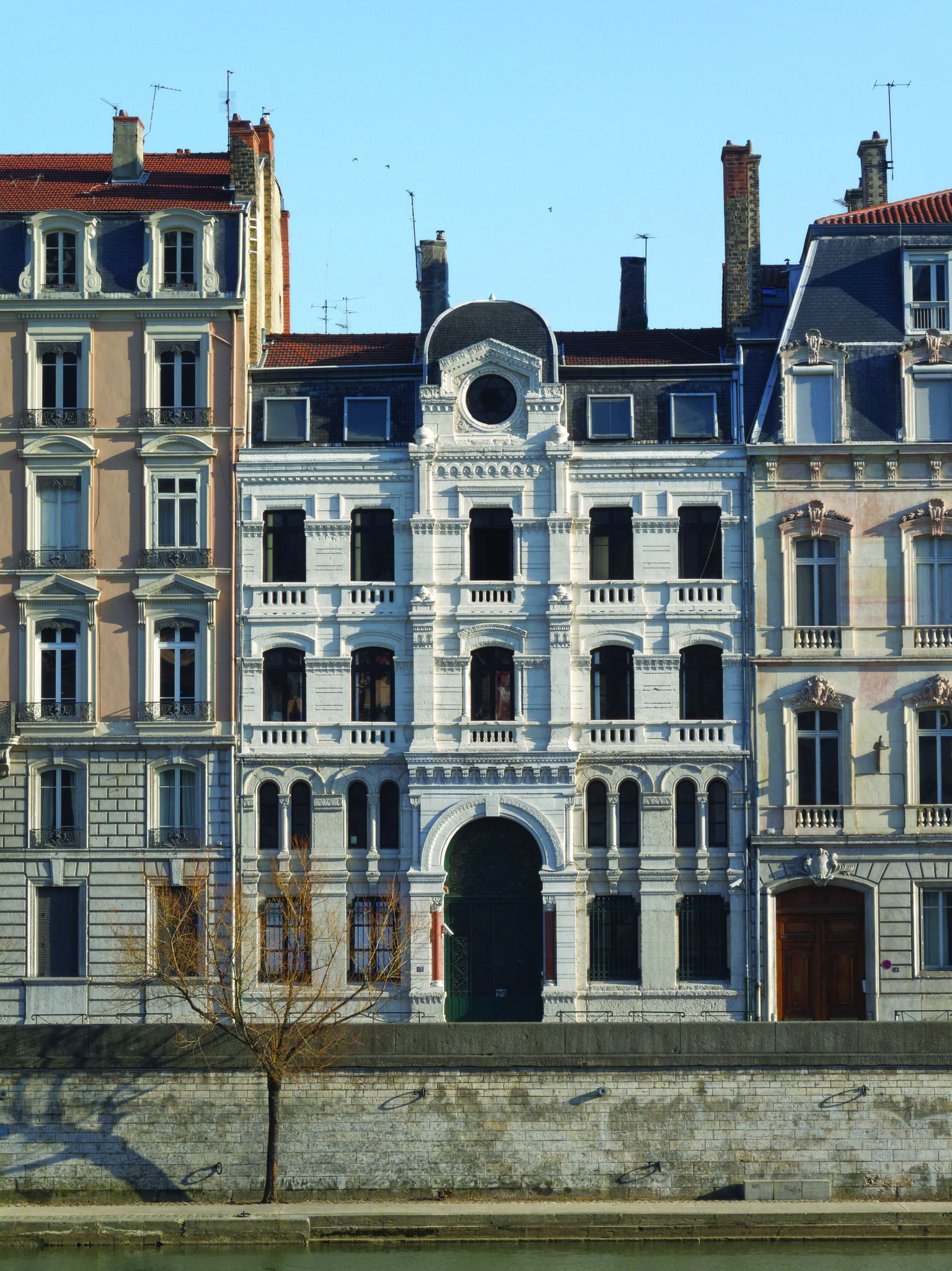 Photography of street view of buildings with low stone wall in front. 