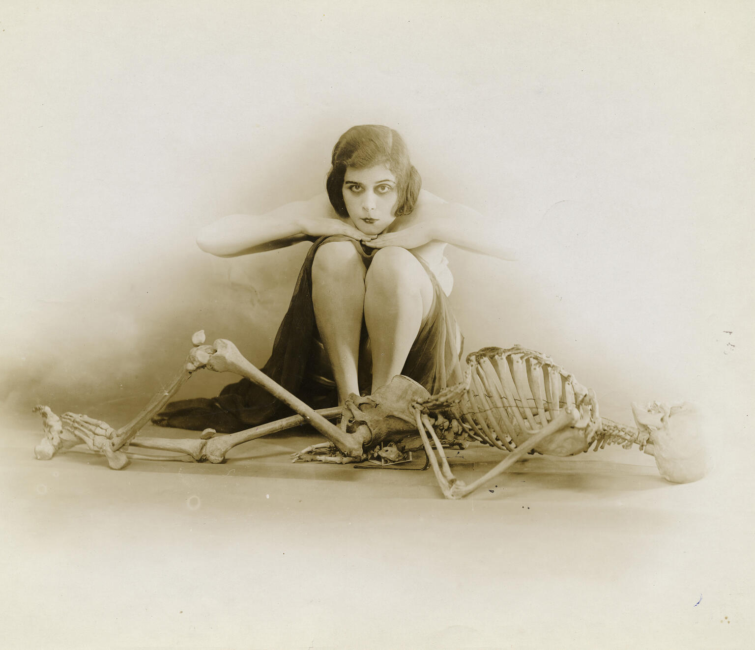 Photograph of female figure sitting behind skeleton.
