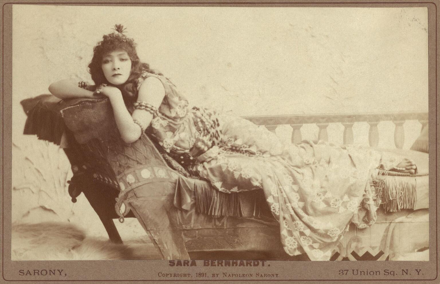 Photograph of woman lying on chaise lounge facing viewer.
