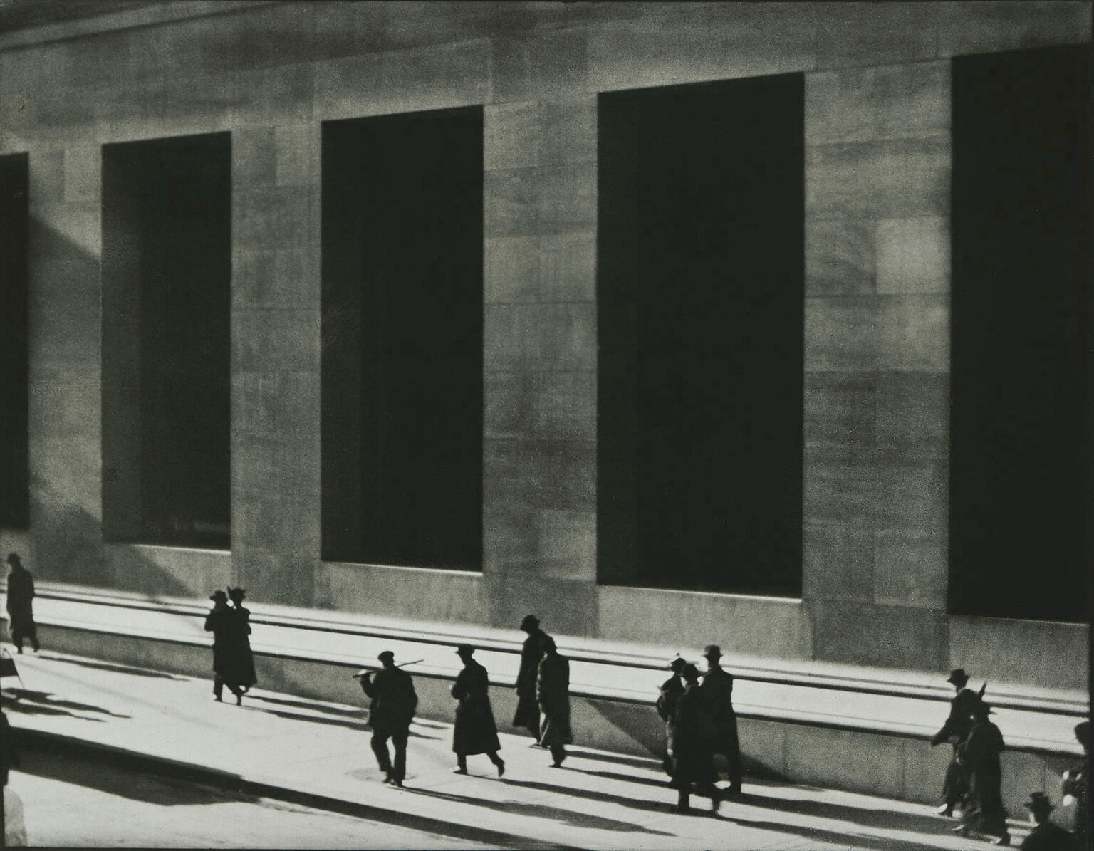 Photograph of silhouetted men walking next to high-columned building.