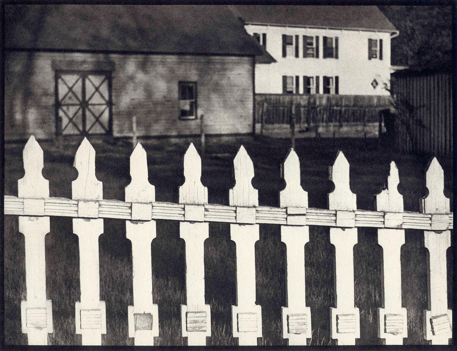 Photograph of fence in foreground and two houses in background.