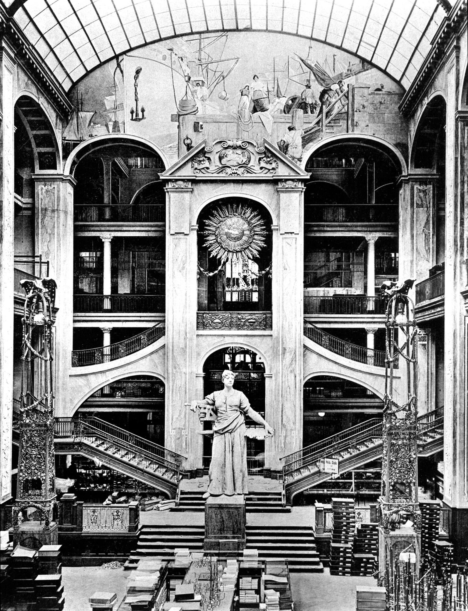 Photograph depicting tall statue in the center of large atrium with interior staircases.