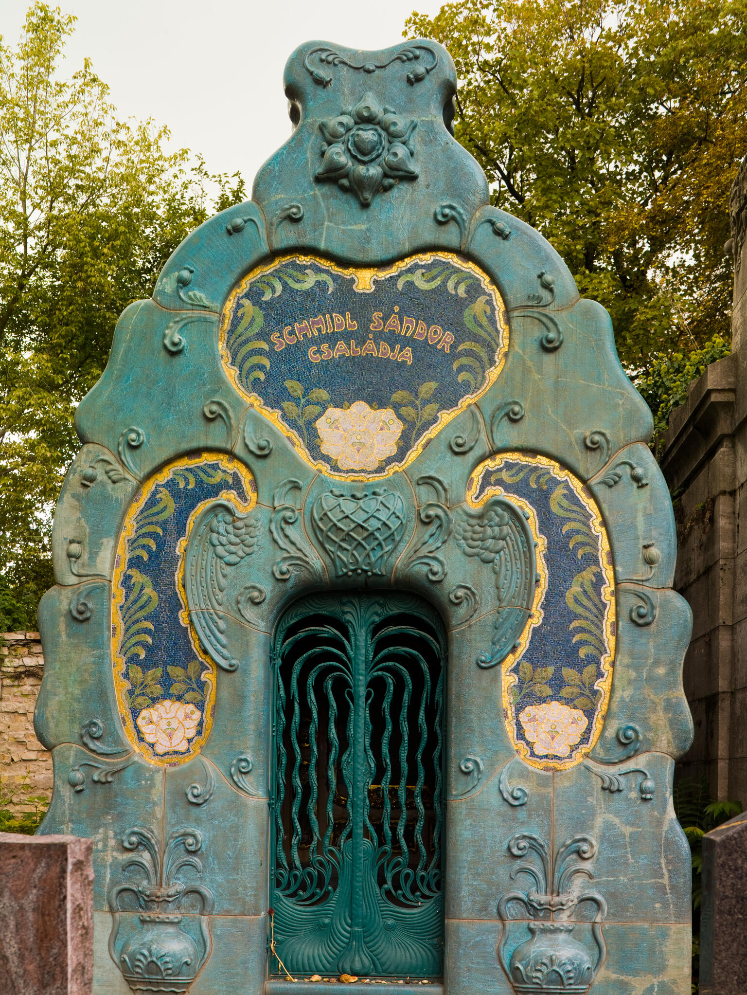 Photograph of gated door outside, surrounded by large archway and decorative floral motifs.