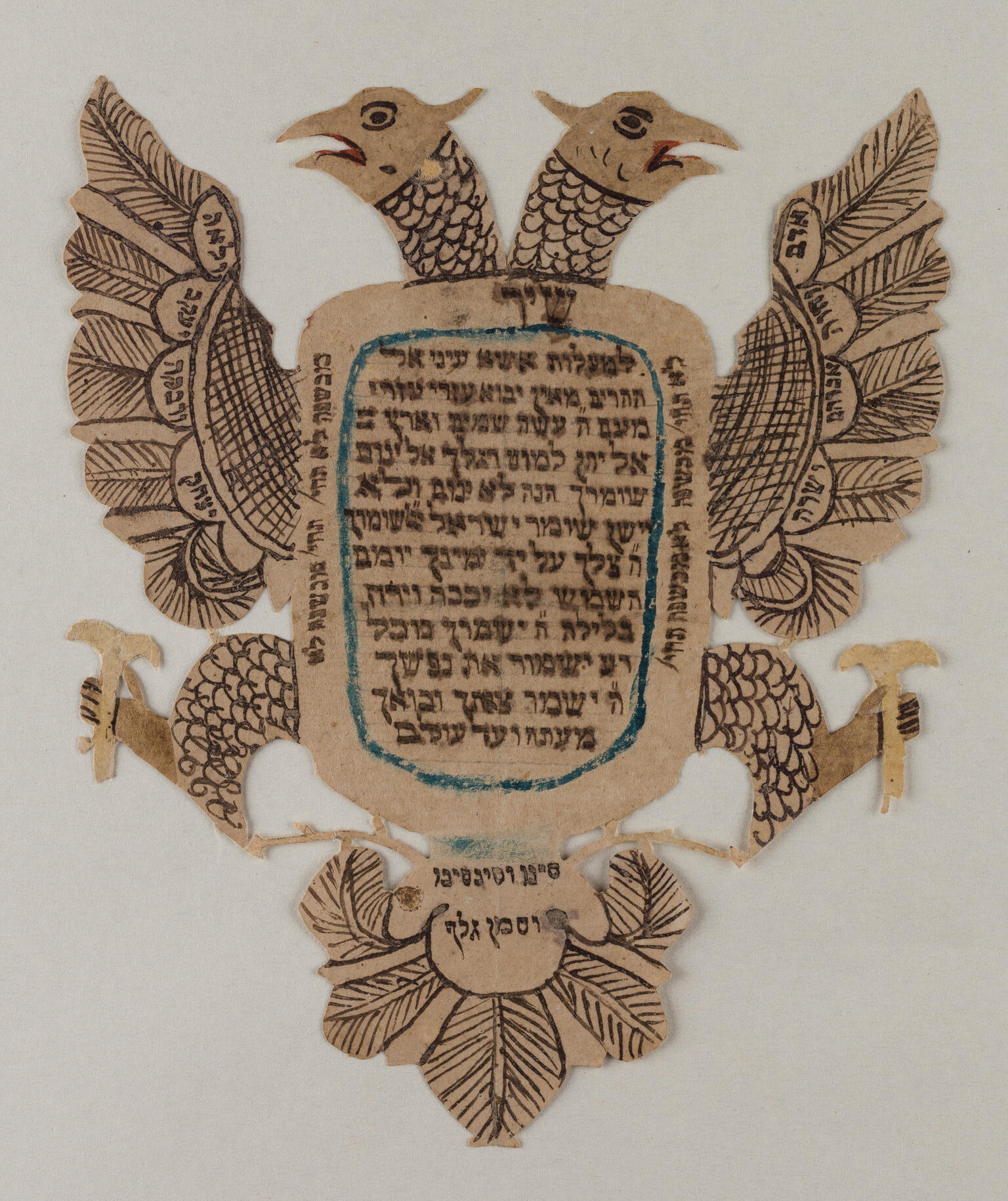 Paper cut in the shape of a two-headed eagle with spread wings, filled with Hebrew writing.