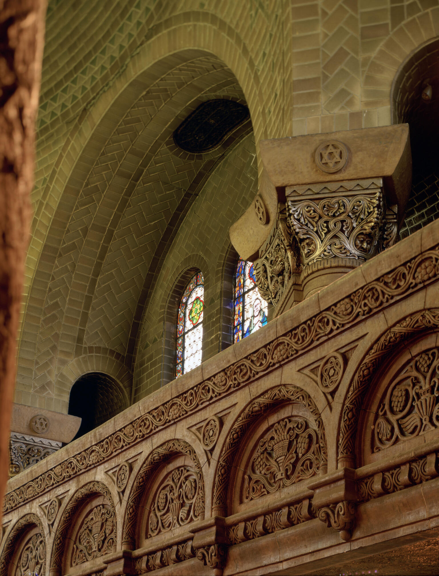 Photograph of stained glass window arch with smaller arches underneath with etchings of floral designs, leaves, and fruit. Photograph of stained glass window arch with smaller arches underneath with etchings of floral designs, leaves, and fruit.