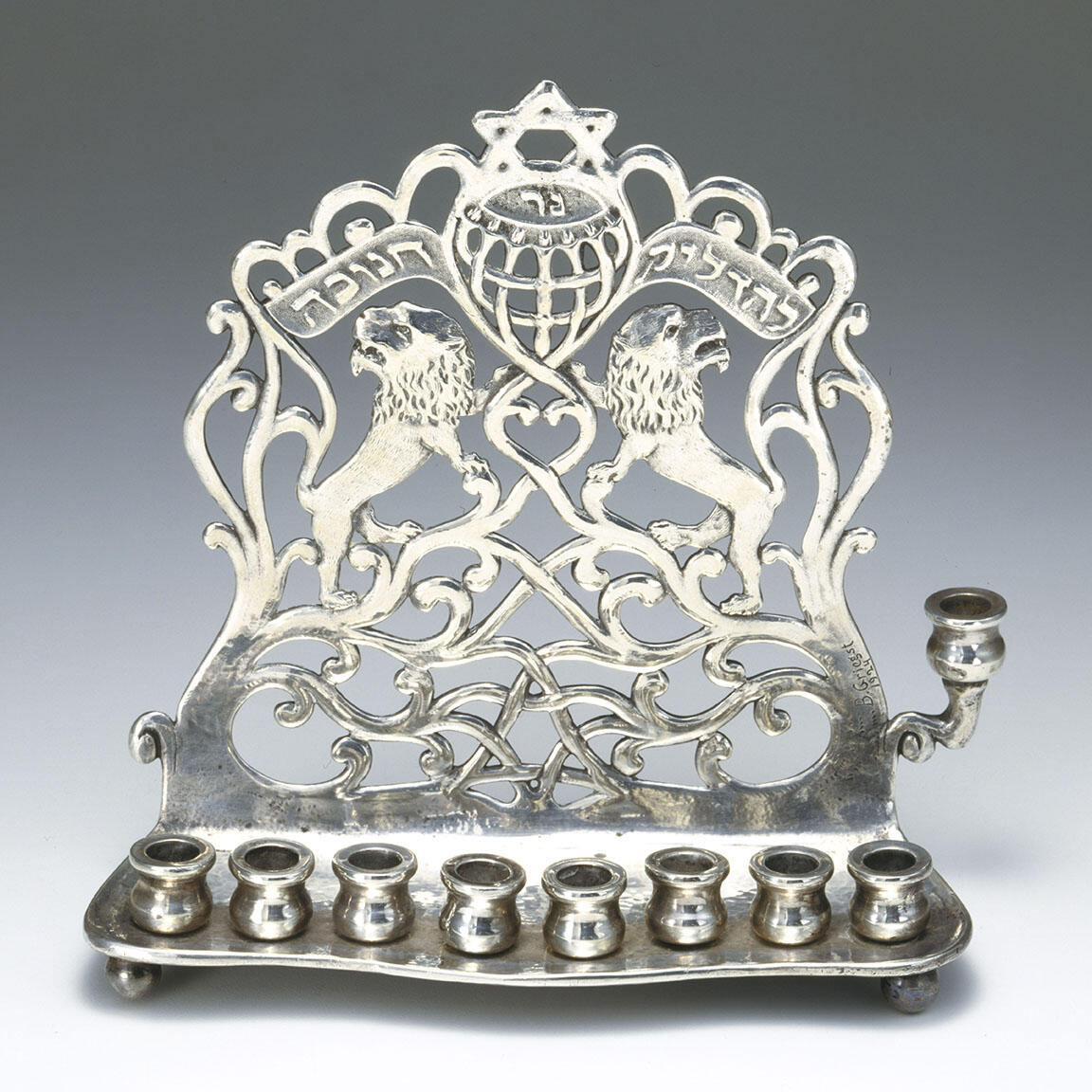 Eight-branched candelabrum with backplate with lions, a Hebrew inscription, Stars of David, and a scalloped top edge. 