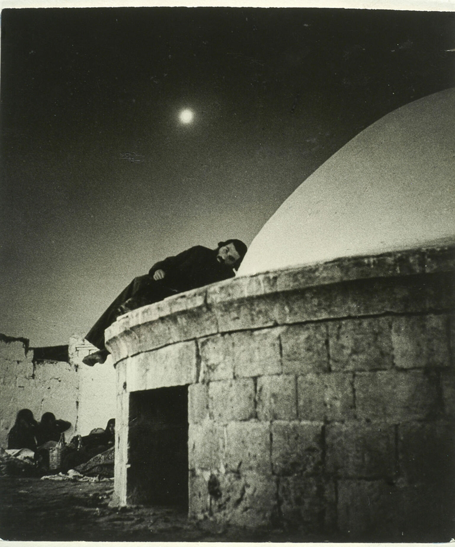 Photograph of man lying on domed roof of stone building. Photograph of man lying on domed roof of stone building.