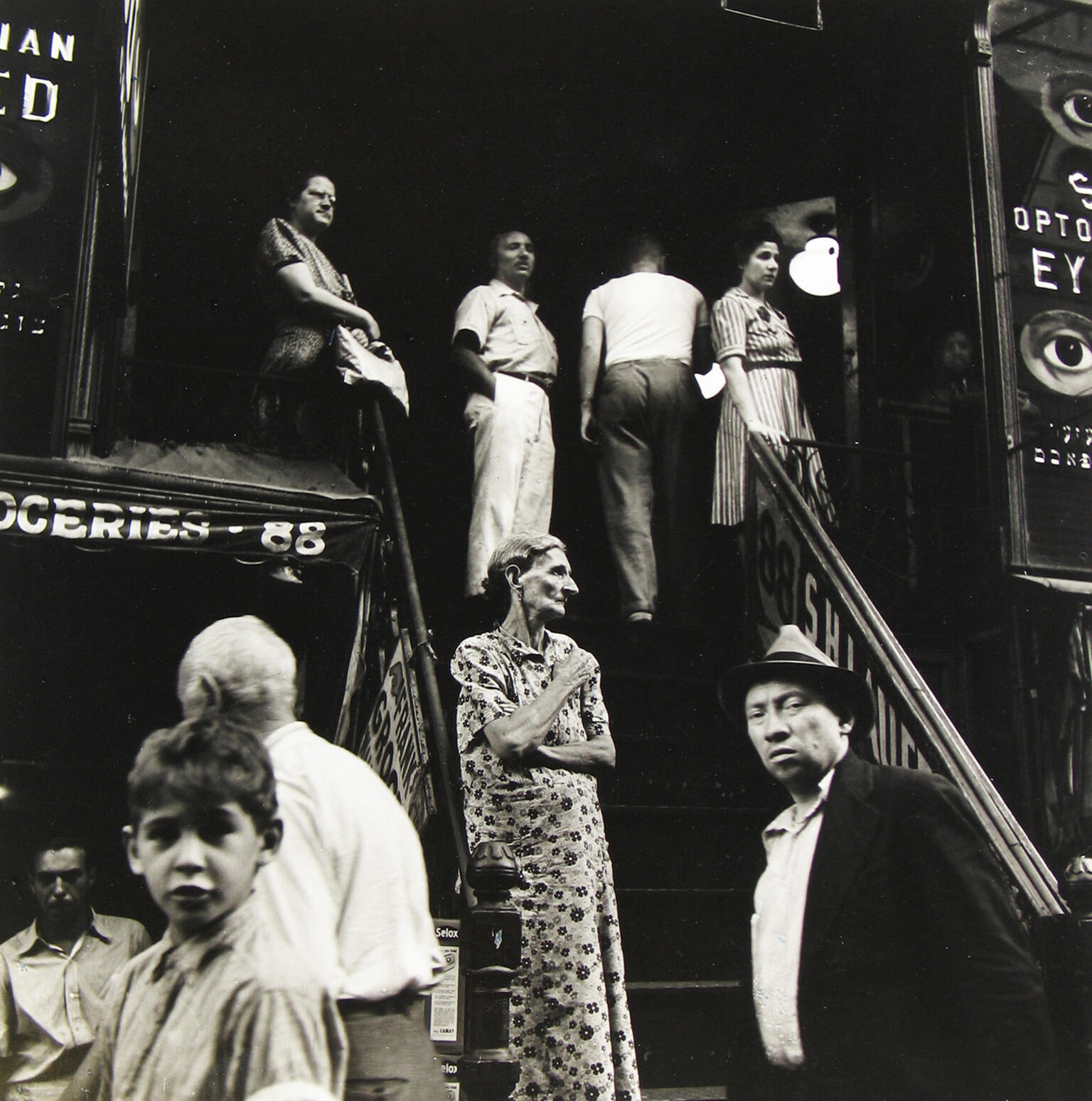 Photograph of people standing outside along stairwell and storefronts. Photograph of people standing outside along stairwell and storefronts.
