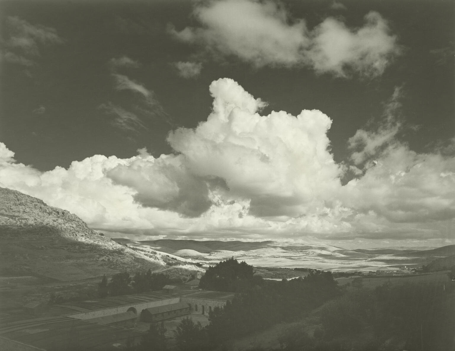 Photograph of valley with buildings under cloudy sky.