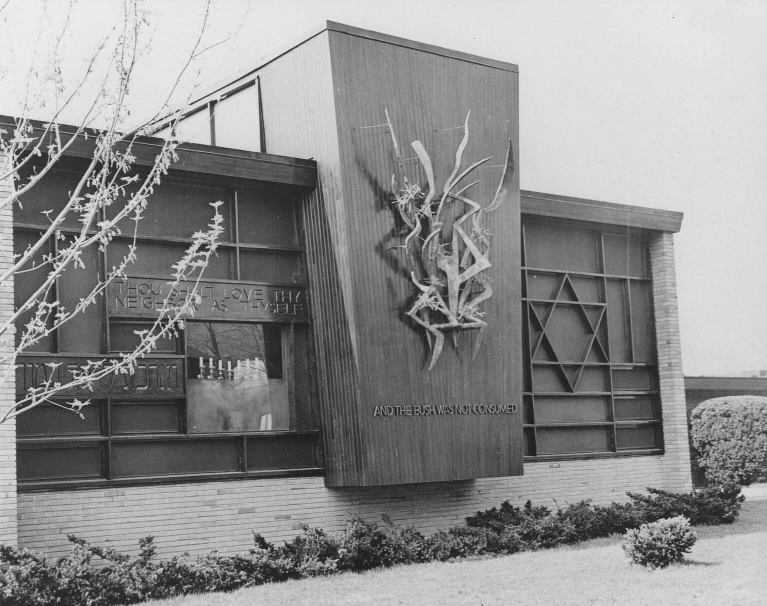 Exterior wall of synagogue featuring Star of David on the right side of the wall and a ribbon-like sculpture in the middle of the wall on a prominent vertical section that juts out from the rest of the wall, with inscription in English reading "And the bush was not consumed."