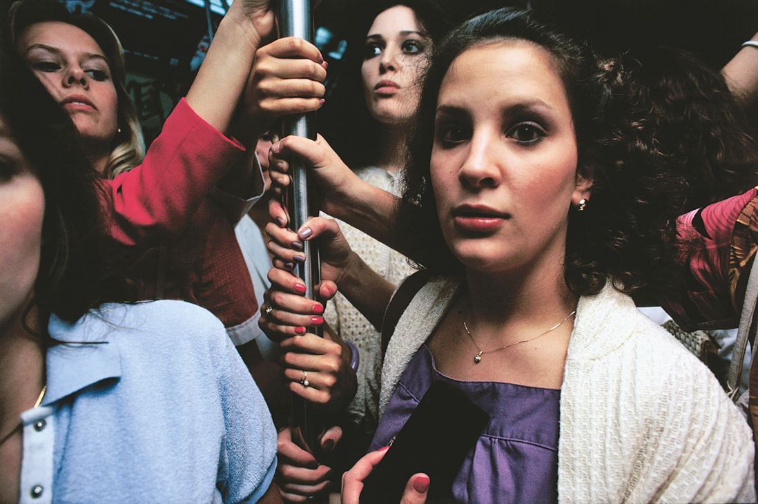 Photograph featuring women standing holding on to a subway pole. Photograph featuring women standing holding on to a subway pole.