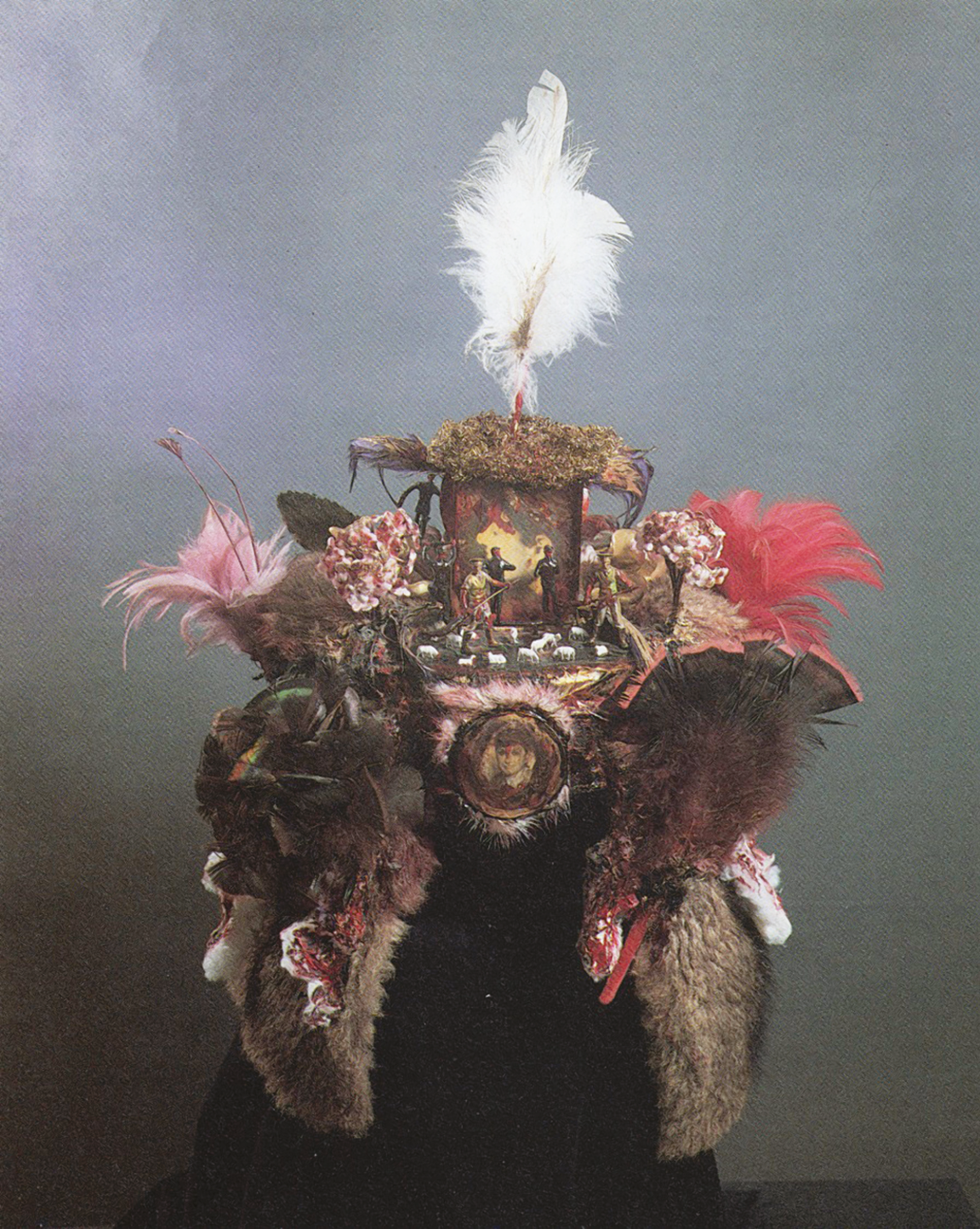 Assemblage of feathers, photographs, and figurines of humans and animals in a hat shape. Assemblage of feathers, photographs, and figurines of humans and animals in a hat shape.