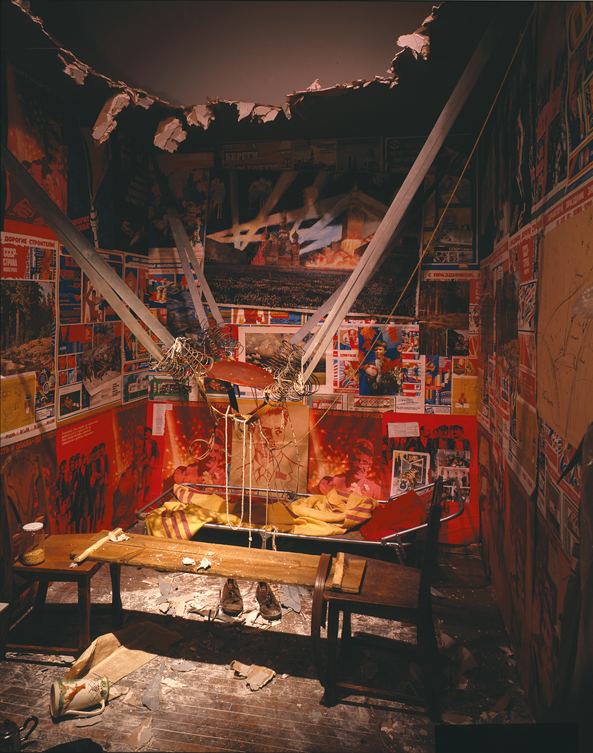Installation featuring catapult-like contraption in the middle strung between two walls, a hole in the ceiling, and scientific drawings and posters on the walls. 