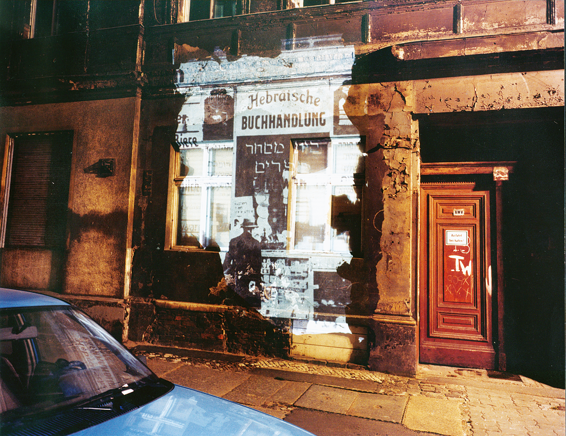 Photograph of blank city wall with projection of storefront over it and car in foreground. Photograph of blank city wall with projection of storefront over it and car in foreground.