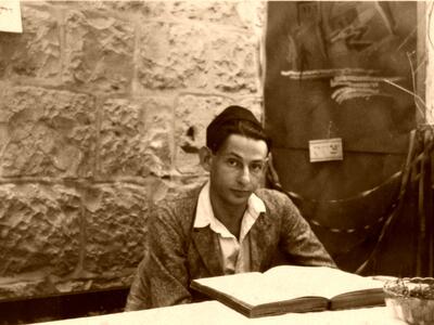 A man wearing a kippah sits at a table with an open book in front of him.