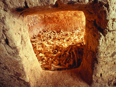Rectangular window within stone tomb revealing cache of many human bones.