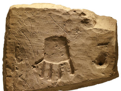 Stone piece with carving of small hand with fingers pointing downward and Hebrew inscription.