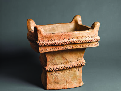 Square ceramic altar with recessed offering surface decorated with crosshatching and circles and horns on four upper corners.