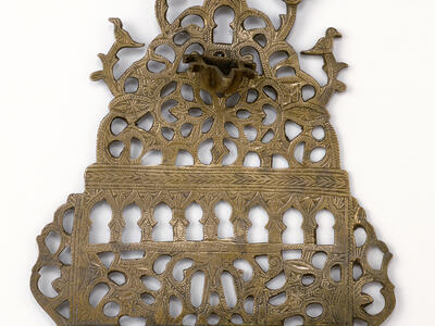 Oil lamp with cut-outs in various shapes, with row of eight cups on bottom and one cup on top. 