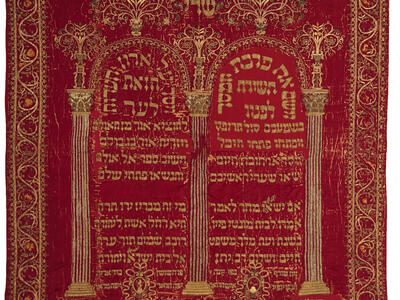 Cloth embroidered with Hebrew writing under columned archway and surrounded by decorative border. 