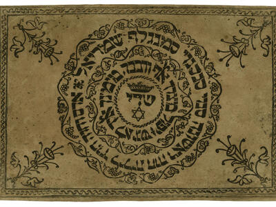 Printed page with Hebrew text in a circle framed by decorative motif with flower in each corner.
